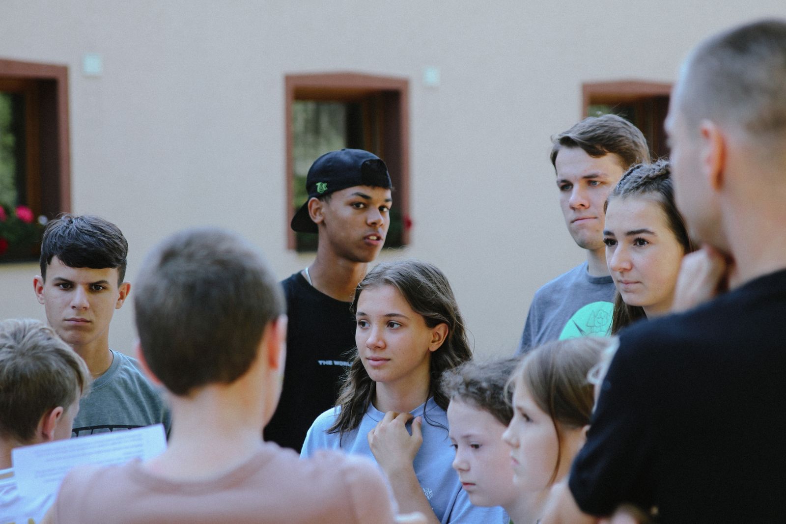 A diverse group of teenagers gathered outdoors, listening and taking part in a youth group discussion